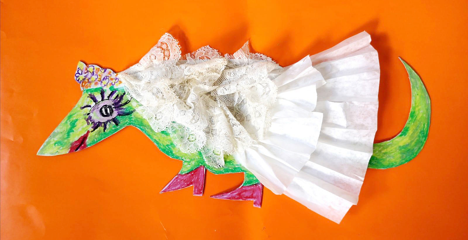 Es ist ein gezeichneter grüner Drache mit einem weißen Kleid aus echten Stoffen zu sehen.