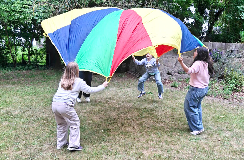 Vier Kinder spielen mit einem großen Tuch, welches sich mit Luft füllt, wenn alle es gemeinsam nach unten ziehen.